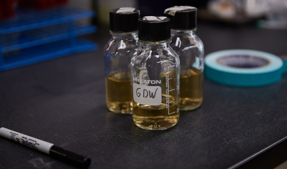Three small bottles filled with yellow liquid are sitting on a counter in a lab.