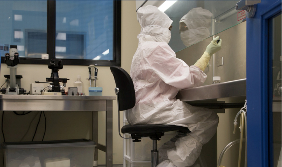 A person in a sterile lab suit works at a lab bench