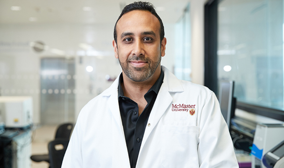 A smiling man wearing a lab coat that says McMaster University