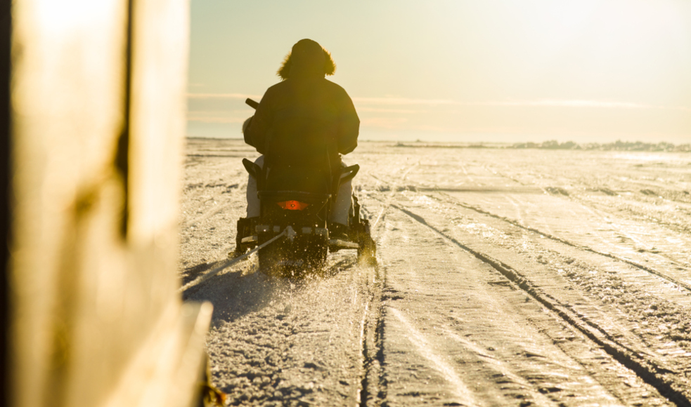 A person in a parka rides a snomobile across a frozen lake