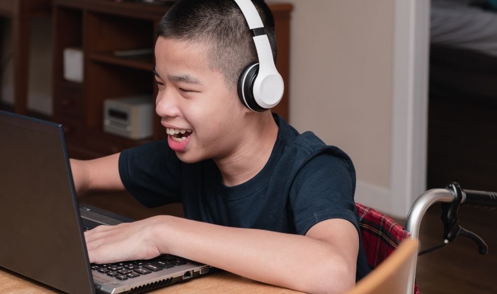 A kid with headphones smiling at a laptop
