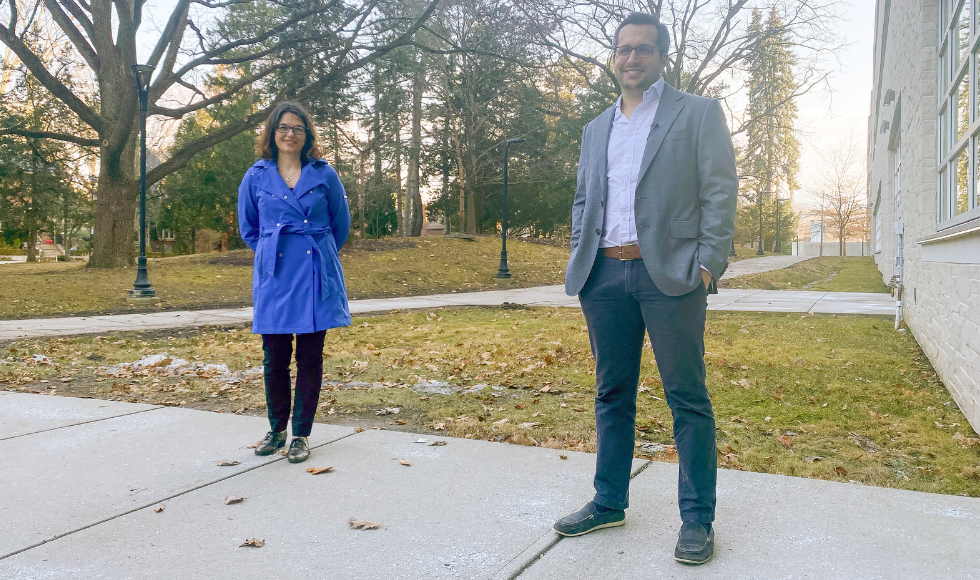 McMaster researchers Dawn Bowdish and Andrew Costa stand outdoors, several feet apart from one another, and smile at the camera.
