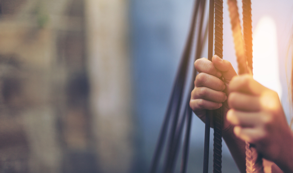 two hands holding bars in an industrial building, light shining through.