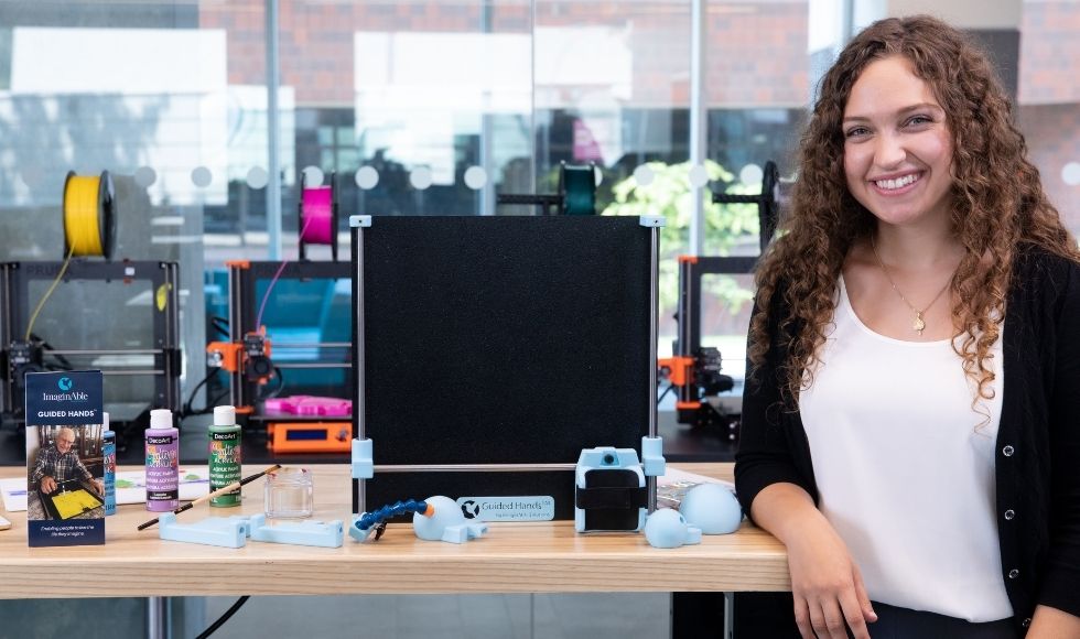 Smiling Lianna Genovese leaning against a table with her device on it.