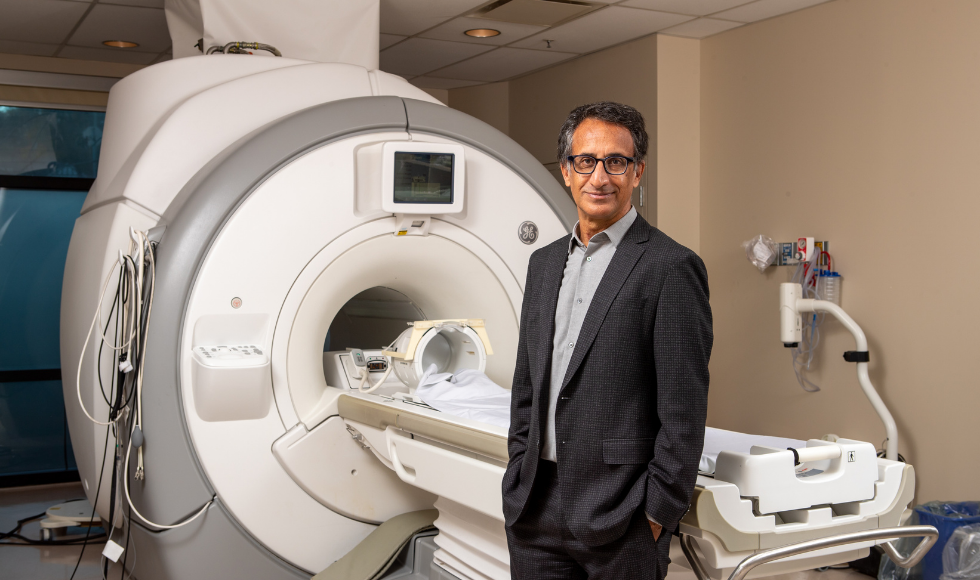 Parminder Raina stands beside a MRI machine in a clinical space.