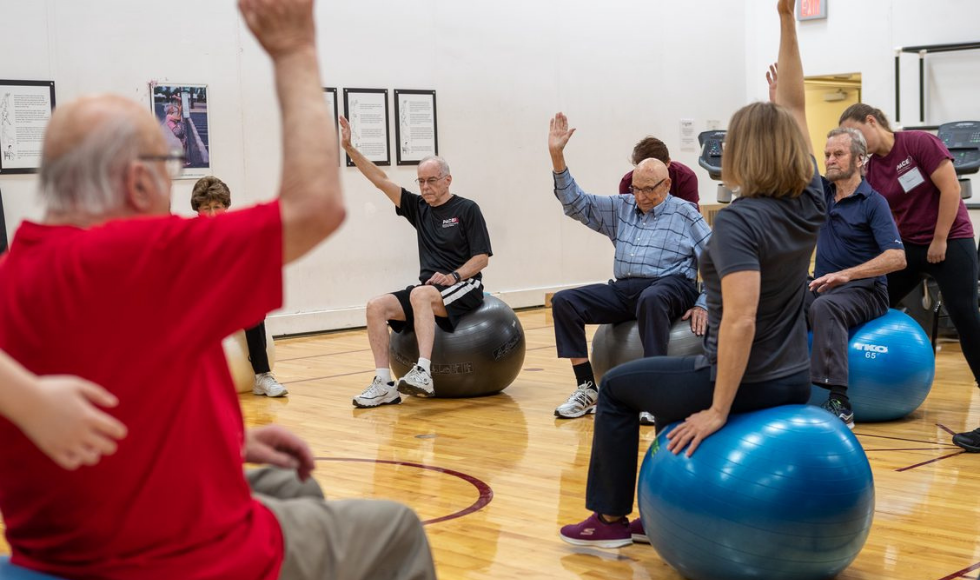 A group of older adults exercises indoors using Pilates balls.