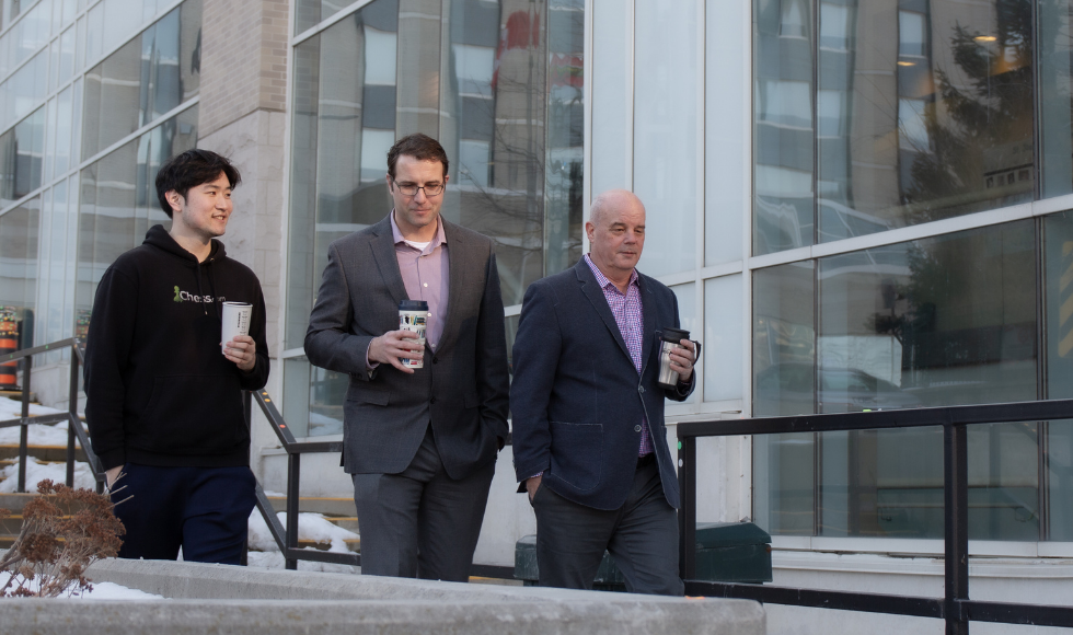 Three men walking down a staircase holding coffee cups