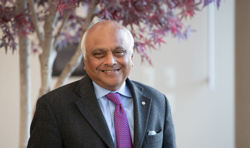 Salim Yusuf smiling at the camera. He is wearing a suit with a blue and fuchsia patterned tie.