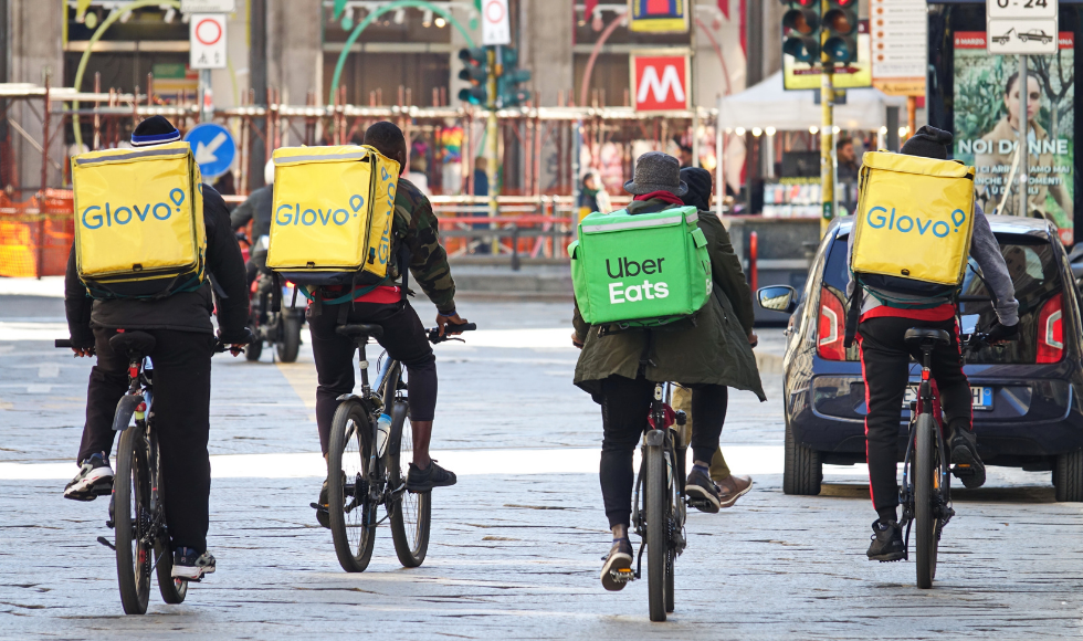 Four food delivery cyclists drive down an urban street