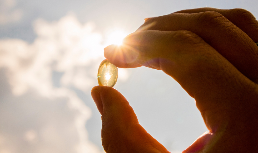 Outdoor closeup of fingers holding a translucent pill up to bright sunlight