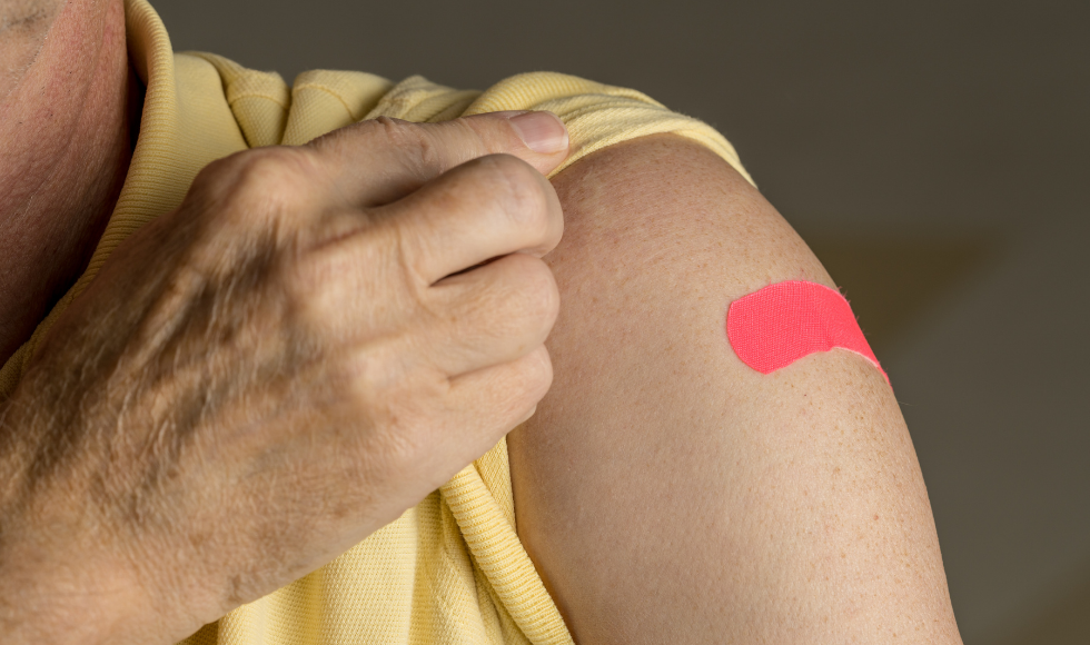 A person holds up their Tshirt sleeve to show a bandaid on their upper arm.