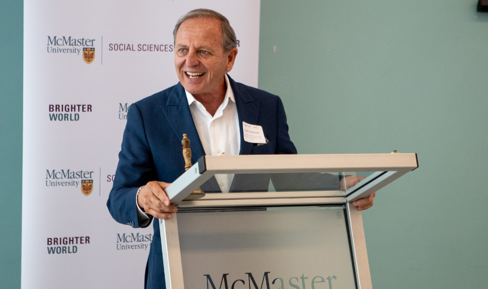 Joseph Mancinelli speaking at a McMaster lecturn in front of a McMaster Social Sciences banner