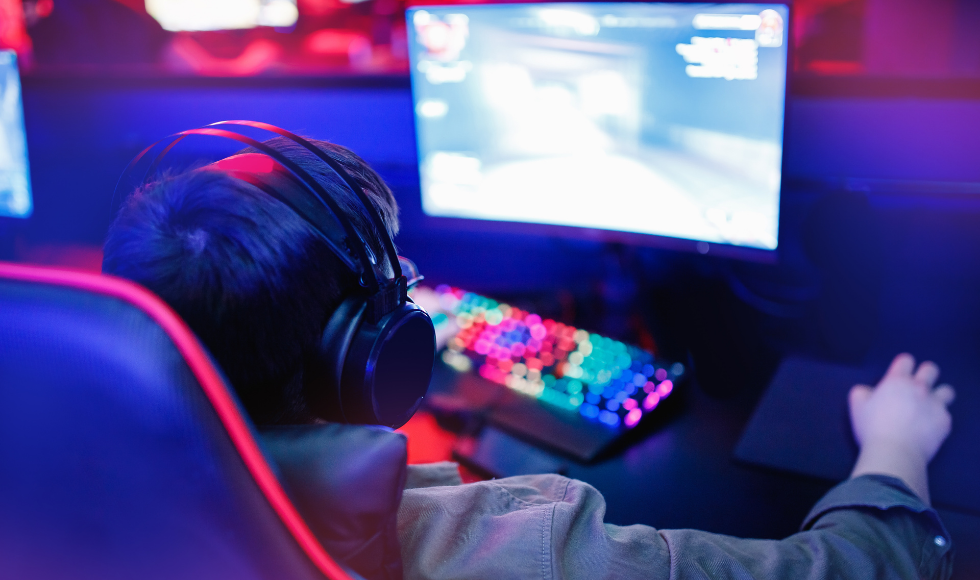 A young gamer sitting with headphones on in front of a computer screen