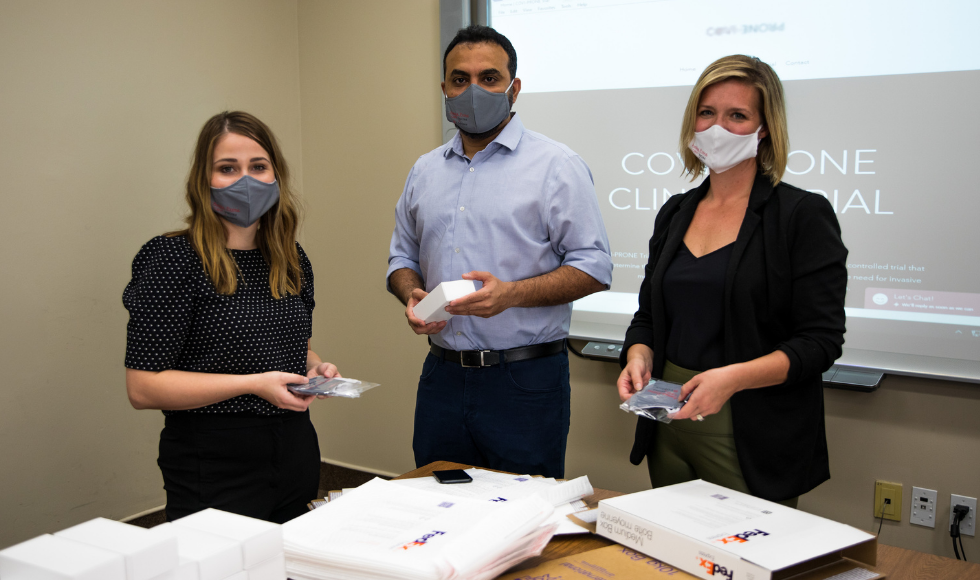 Three masked researchers standing in front of a table that has opened FedEx packages sitting on it ￼