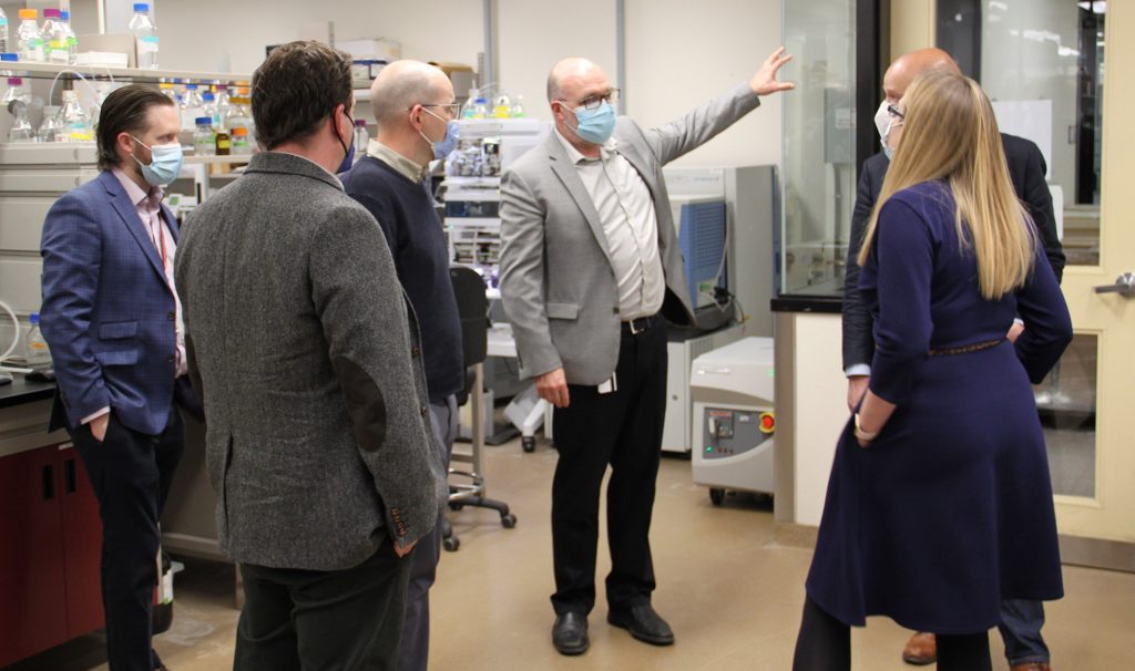 A group of masked people in work clothes getting a tour of a lab