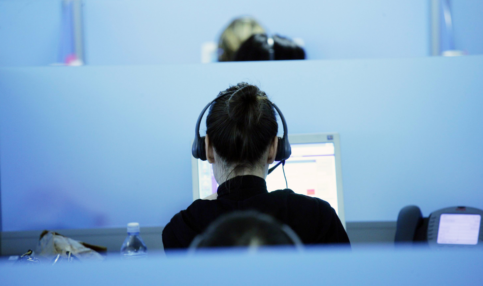 The back of a woman's head as she sits in a cubicle with headphones on