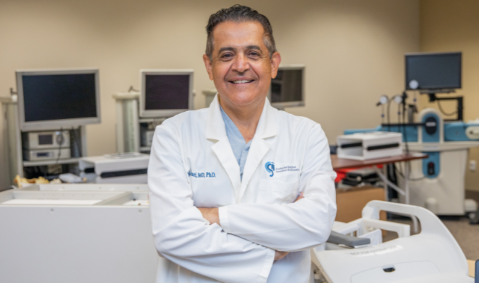 Mehran Anvari in a lab, wearing a lab coat and smiling with his arms crossed.