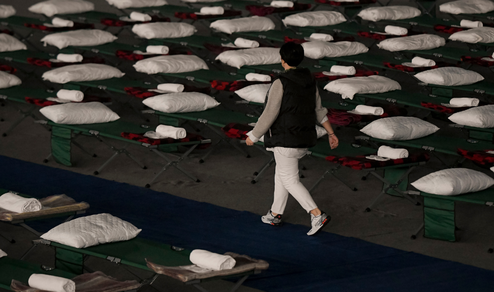 A person walks between rows and rows of temporary cots with a pillow and towel on each, at a refugee camp in Hungary