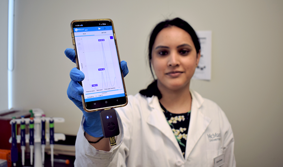Postdoc Richa Pandey holds up a smartphone with test results on the screen.