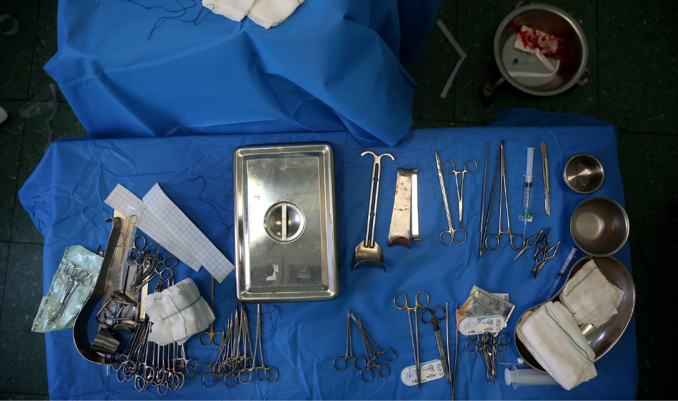 An overhead shot of a table lined with blue fabric. On the table there are many surgical tools, a syringe and gauze.