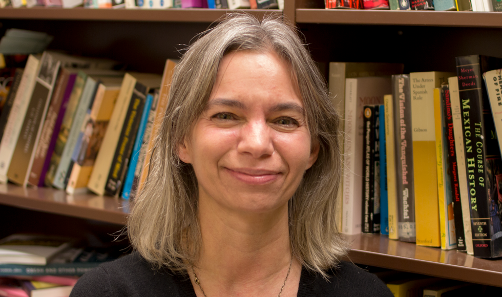 headshot of a smiling Juanita De Barros in front of a bookcase.