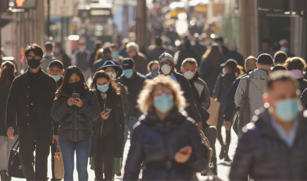 A large group of masked people walking through a busy intersection