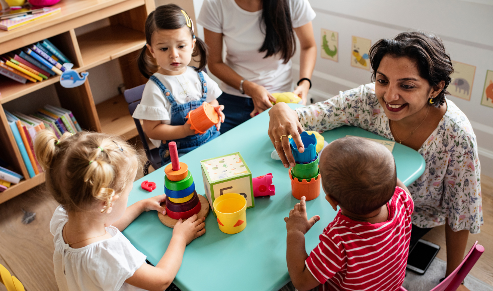 Small chldren playing around a table with an adult supervising