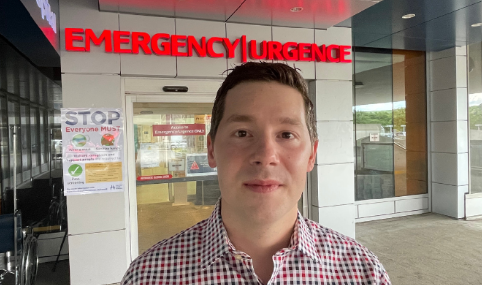 Ryan Strum standing in front of the entrance to an emergency department while looking directly at the camera.