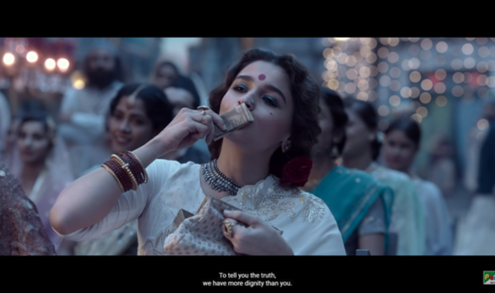 A screen grab from the Bollywood film Gangubai Kathiawadi showing woman holding several pieces of paper money up to her mouth in a kissing motion.
