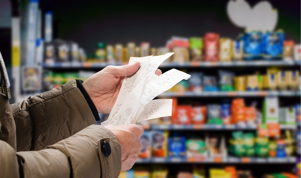 Hands holding a receipt in the foreground against a backdrop of grocery store shelves