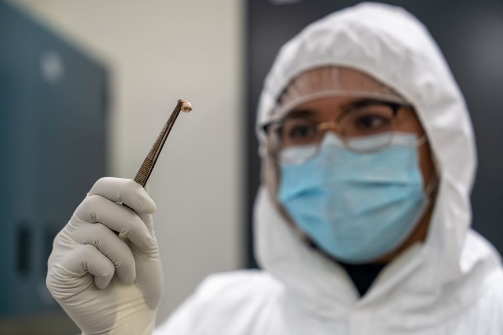 A researcher wearing a protective suit, mask and gloves using a forcep holds up the tooth of someone who died during the Black Death pandemic