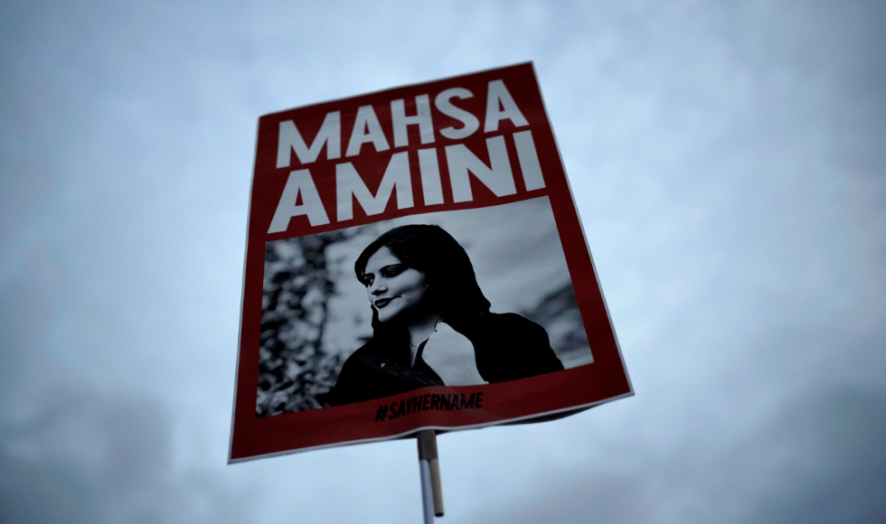 A placard with a picture of Mahsa Amini against a cloudy sky