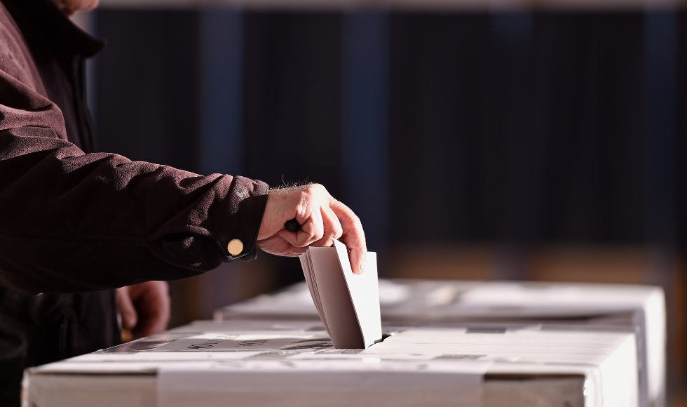 The hand of a voter placing a ballot into a box