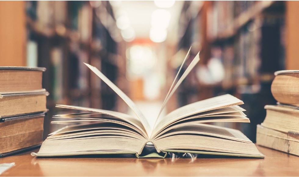 Side view of an open book amid a stack of books in a library.