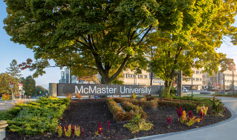 The McMaster University sign surrounded by flowers and trees at the Main Street entrance to campus.