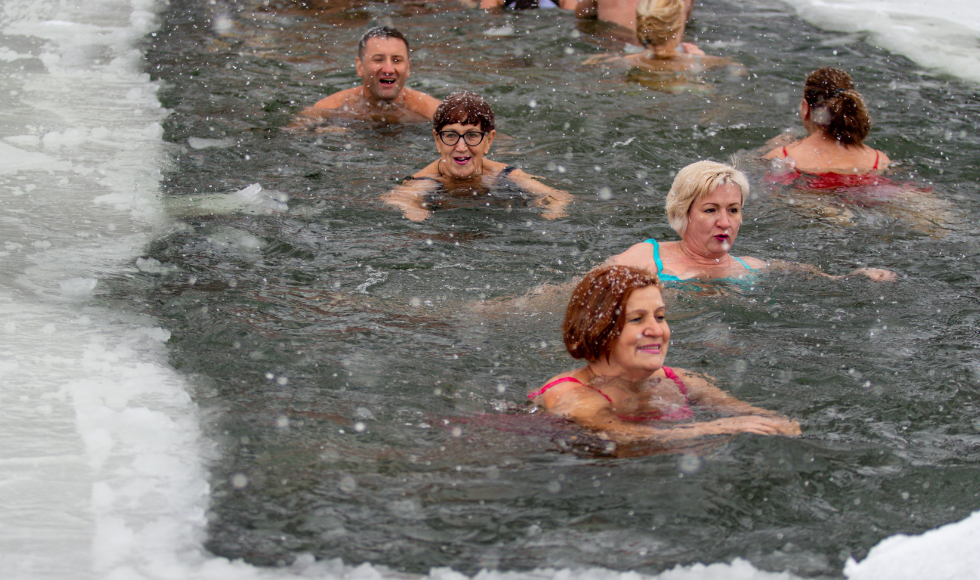 People swim in open water surrounded by a fringe of ice.