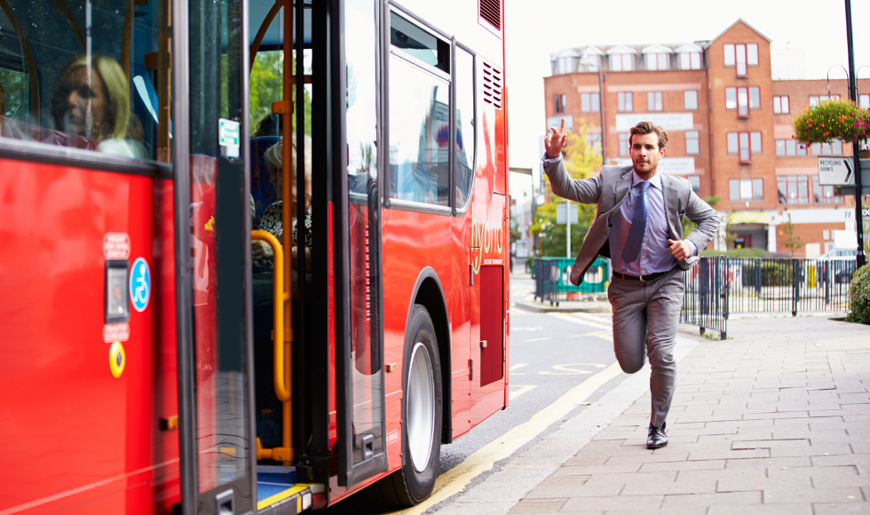 A man in a suit with his arm upraised, running toward a bus.