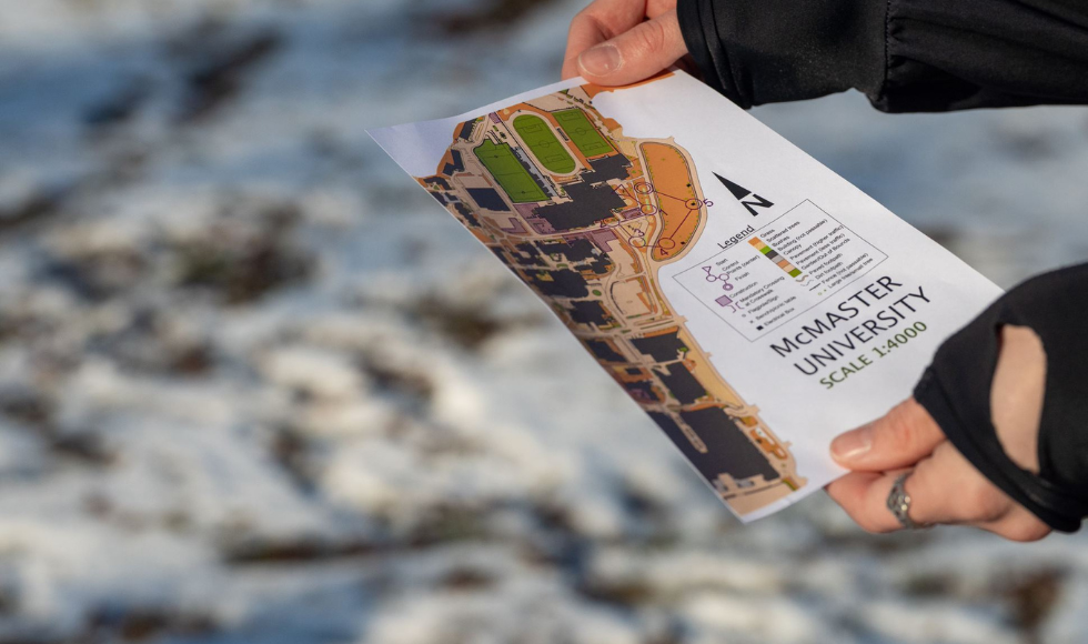 Hands holding a map of McMaster University's campus. A snow-covered patch of grass is in the background.