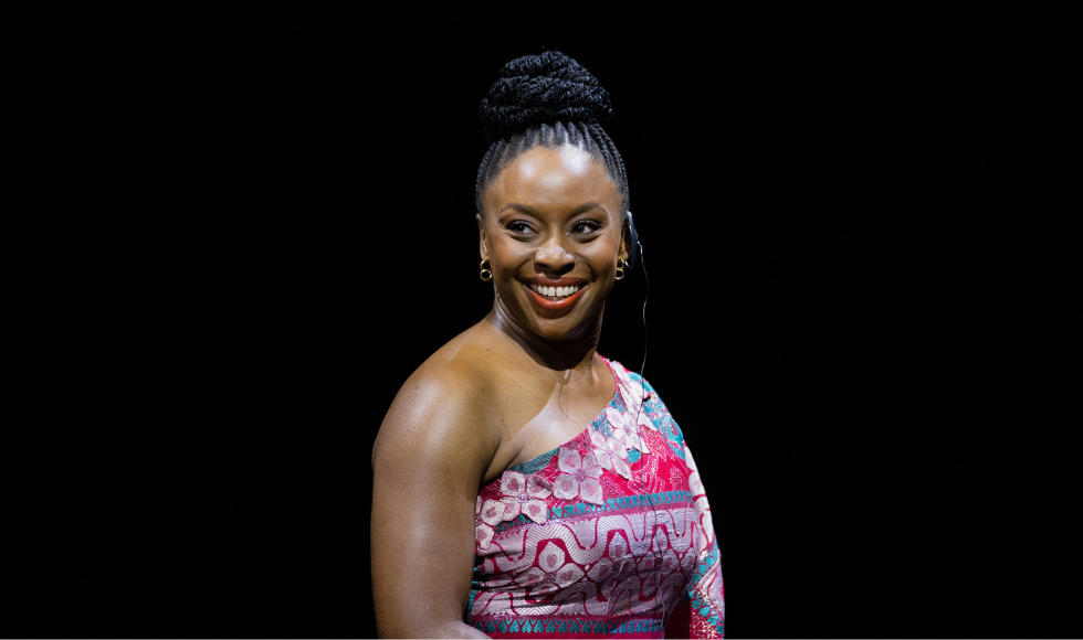 Waist-up image of writer Chimamanda Ngozi Adichie smiling against a black backdrop