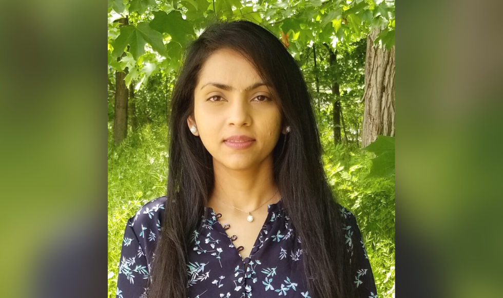 A headshot of Divya Joshi. She is standing outdoors and there is greenery in the background of the photo.