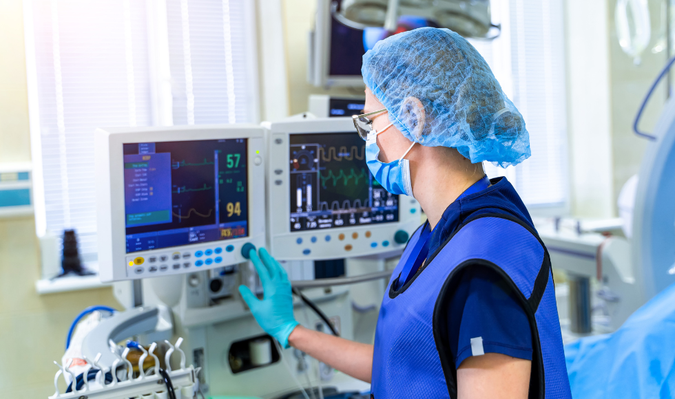 A hospital worker wearing a mask, hair net and medical gloves pressing a button on a medical device.