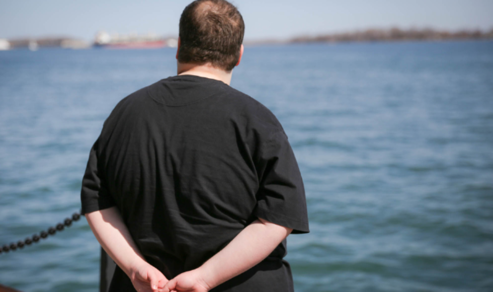 A person in a black t-shirt with their back to the camera looking out at a body of water