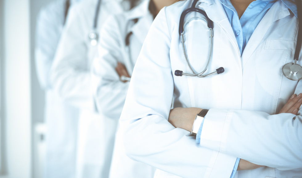 The torsos of four doctors wearing white labours and stethoscopes around their shoulders