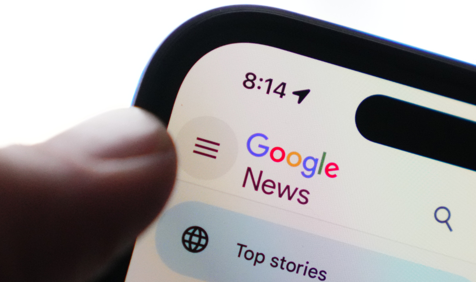 A finger hovering over the corner of a cellphone that has Google News on the screen
