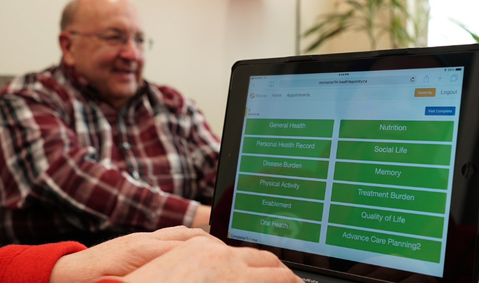 An iPad screen displaying a list of survey topics. In the background there is an older person out of focus.