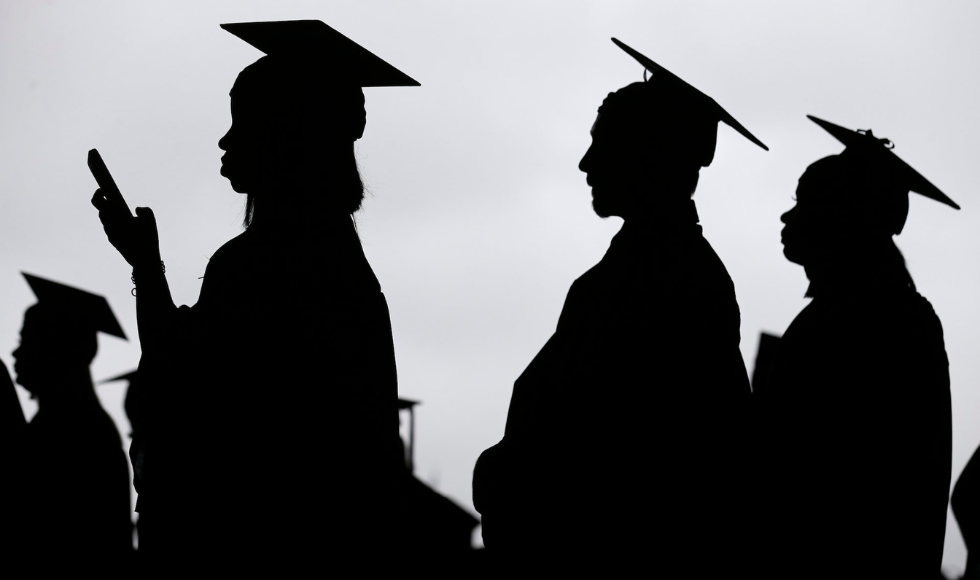 Silhouettes of students in graduation caps. One is holding a phone.