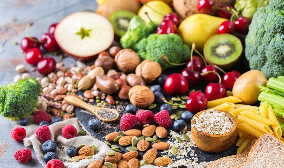 A colourful array of fruit, nuts and vegetables on a grey tabletop.