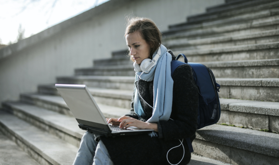 A student sitting on an outdoor staircase working at an open laptop