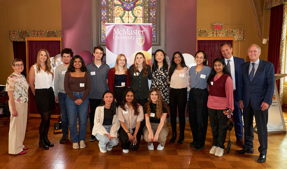 A group of researchers and students posing for a photo in front of a banner bearing the logo of McMaster University