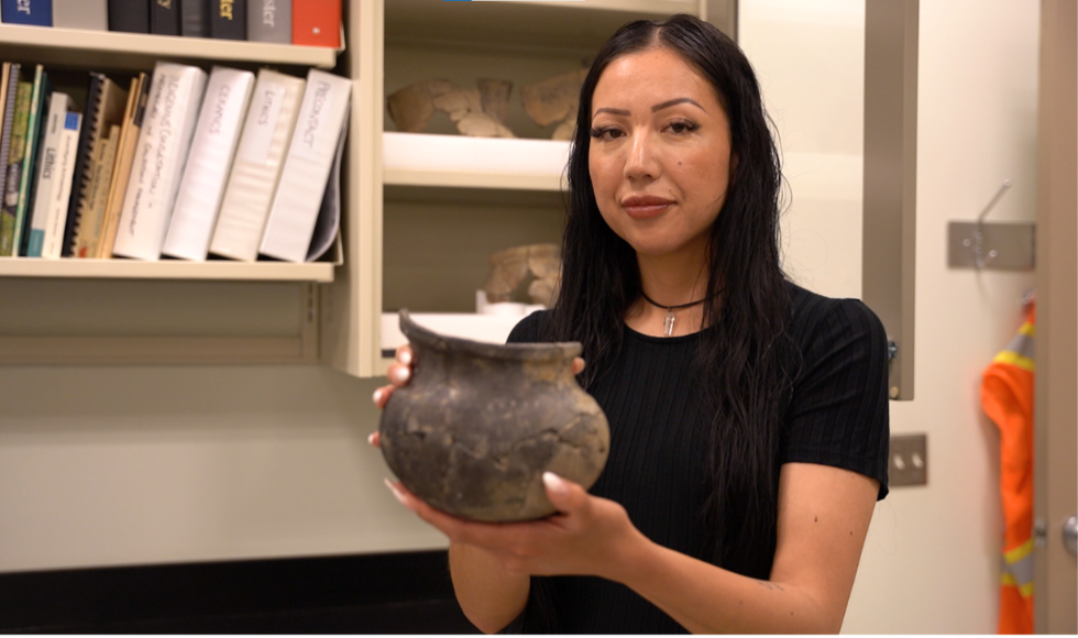 Jackie Porter, a McMaster student, holding a clay cooking vessel from the 16th or 17th century